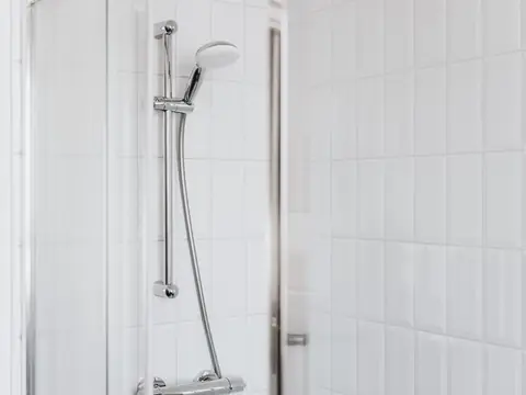 A chrome shower rail and hand shower on white tiles