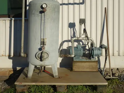A pressure tank and water pump beside a building