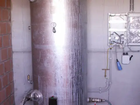 A tall steel water tank with its pipes and gauge