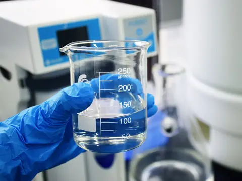 A gloved hand holding a beaker of clear water for a hardness test